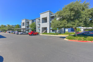 parking lot, covered parking, handicap parking, landscaping, large trees surrounding residential buildings.
