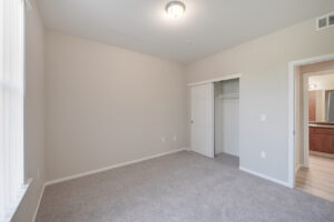 bedroom, window facing bedroom door, neutral toned carpeting, sliding closet door, bathroom across from bedroom